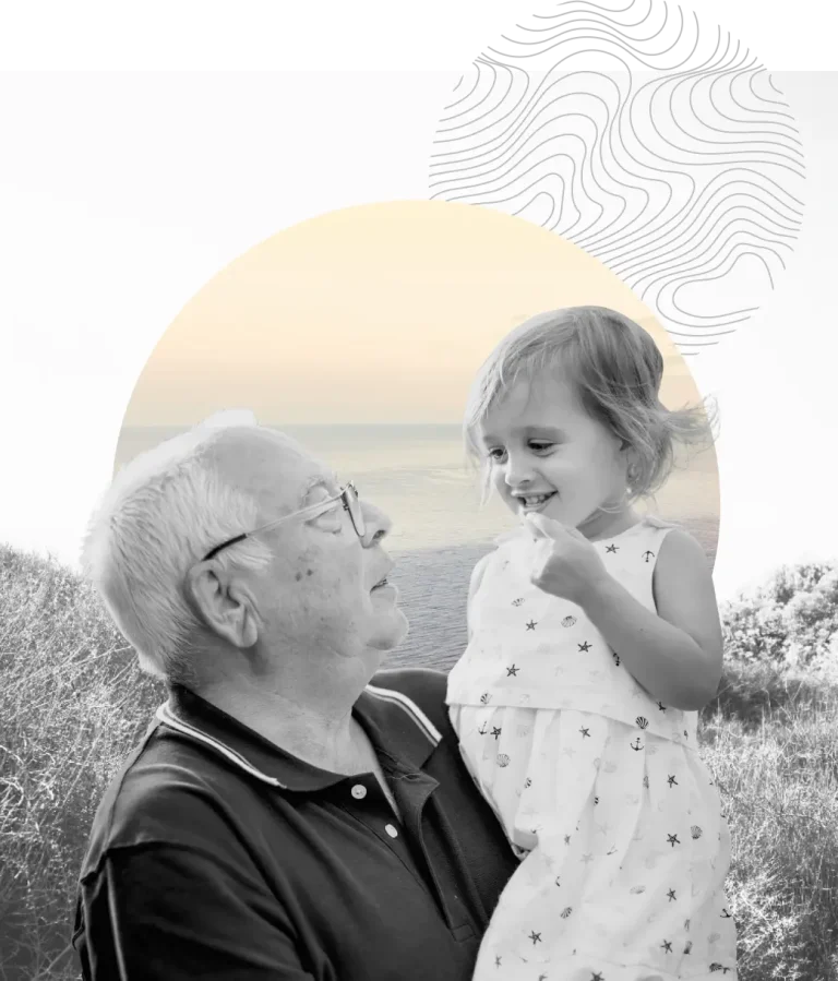 Grandfather holding and smiling at his granddaughter, with an ocean backdrop.