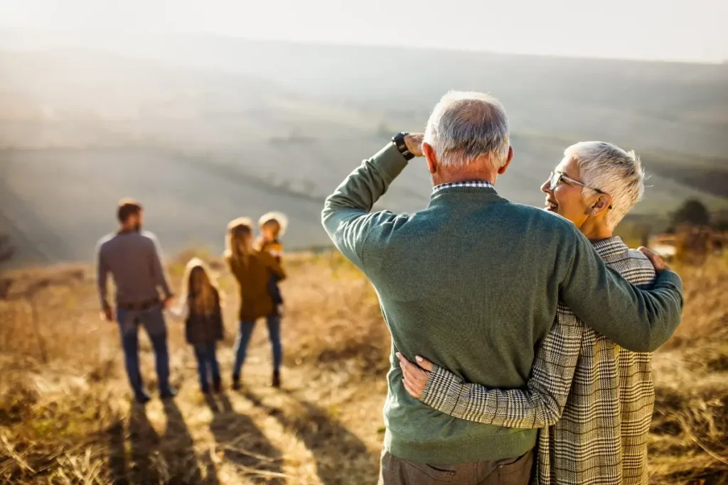 Retired couple embracing while watching their family in a scenic countryside.