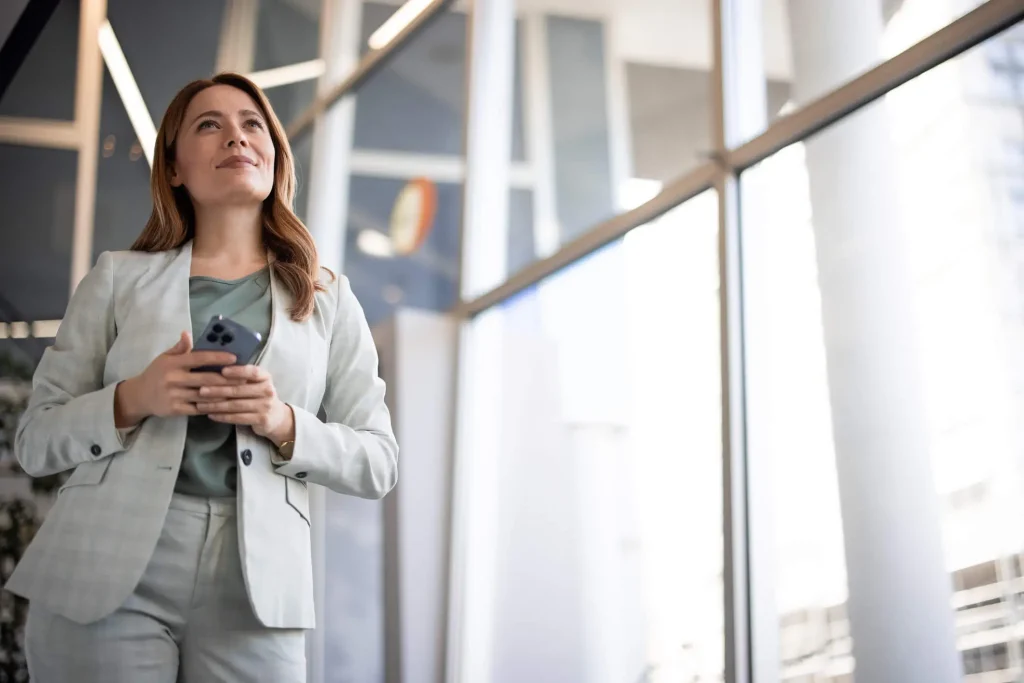 Confident female financial advisor holding a phone and looking ahead in a modern office.