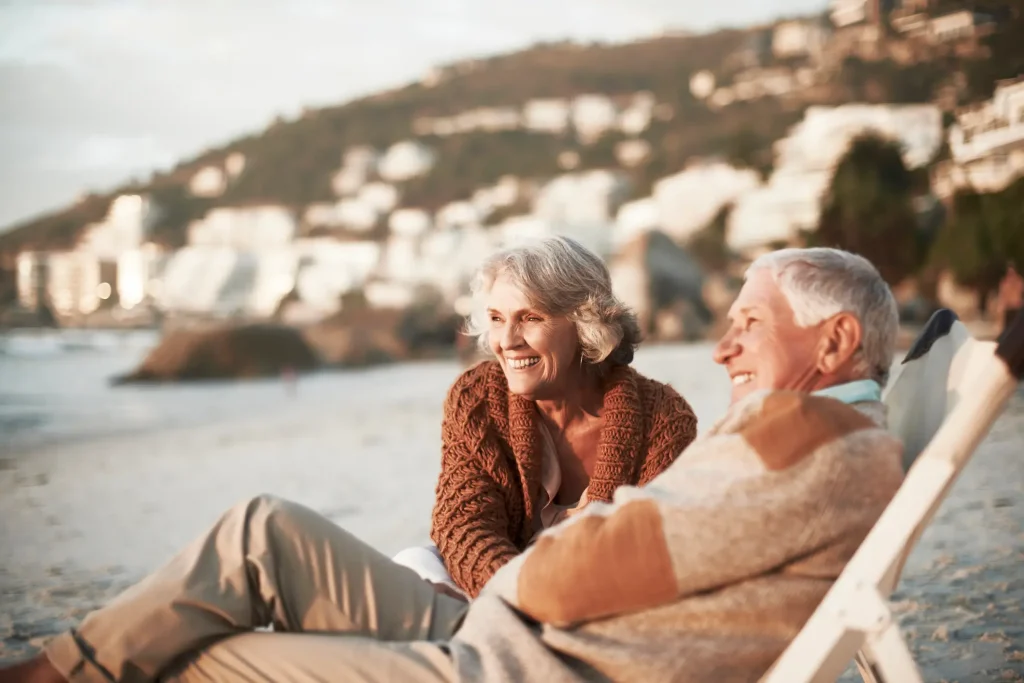 Retired couple smiling and relaxing on a beach.