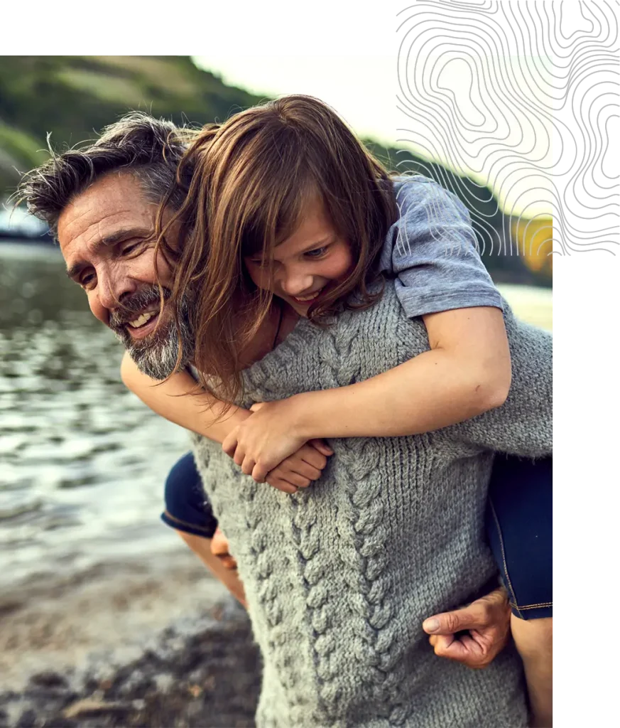 Smiling man giving a young girl a piggyback ride by the water.