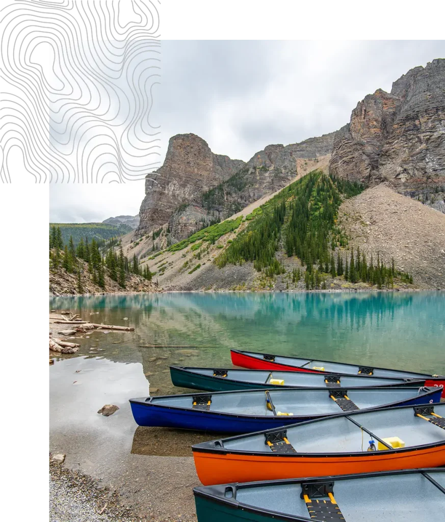 Colorful canoes on the shore of a turquoise lake surrounded by mountains.