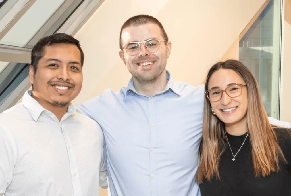 Three Clark Capital teammates smiling and posing together in a modern office setting.